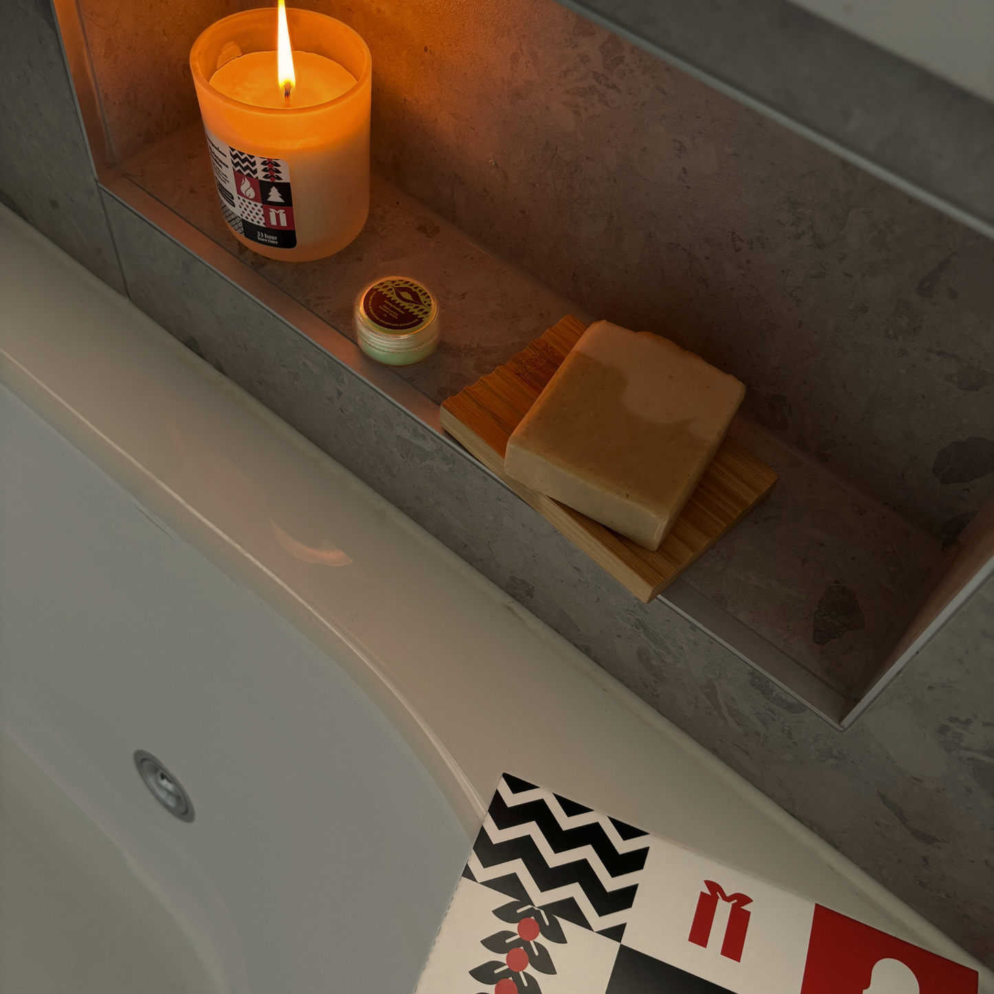 Candle and soap on a ledge next to a bathtub with decorative cards.
