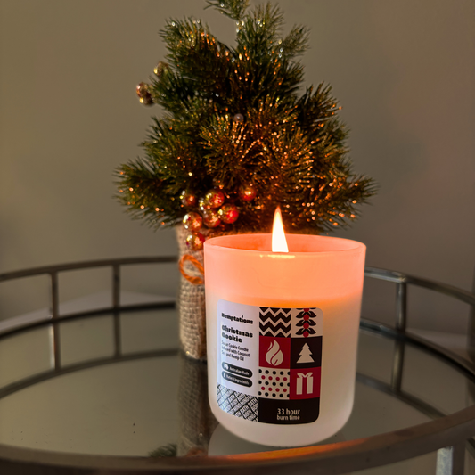 Candle with a decorative label on a glass table next to a small Christmas tree.