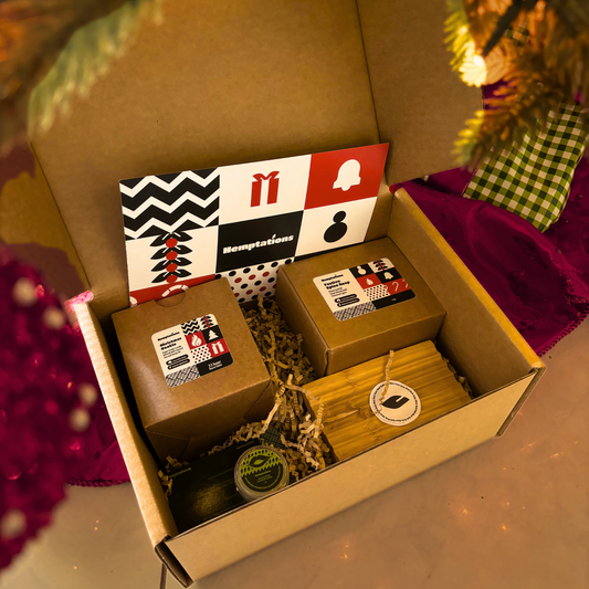 Open cardboard box with gift items including a small bag, a box, and a tube of cream, with a decorative background.