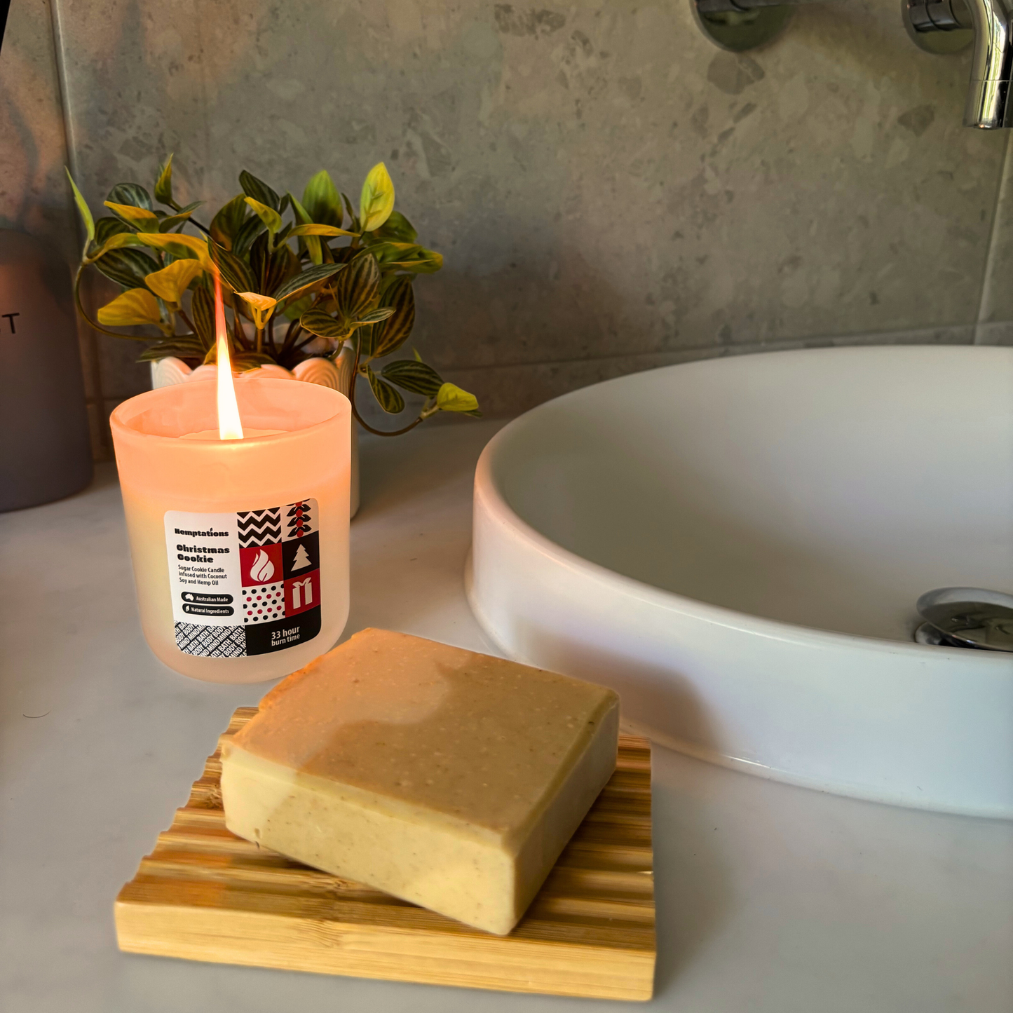 Candle with a label and bar of soap on a wooden stand next to a sink.