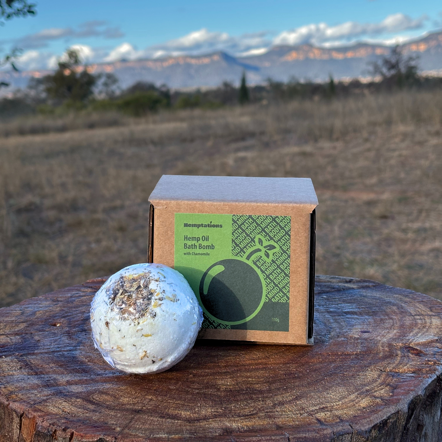 Bath bomb and packaging on a wooden stump with a scenic background