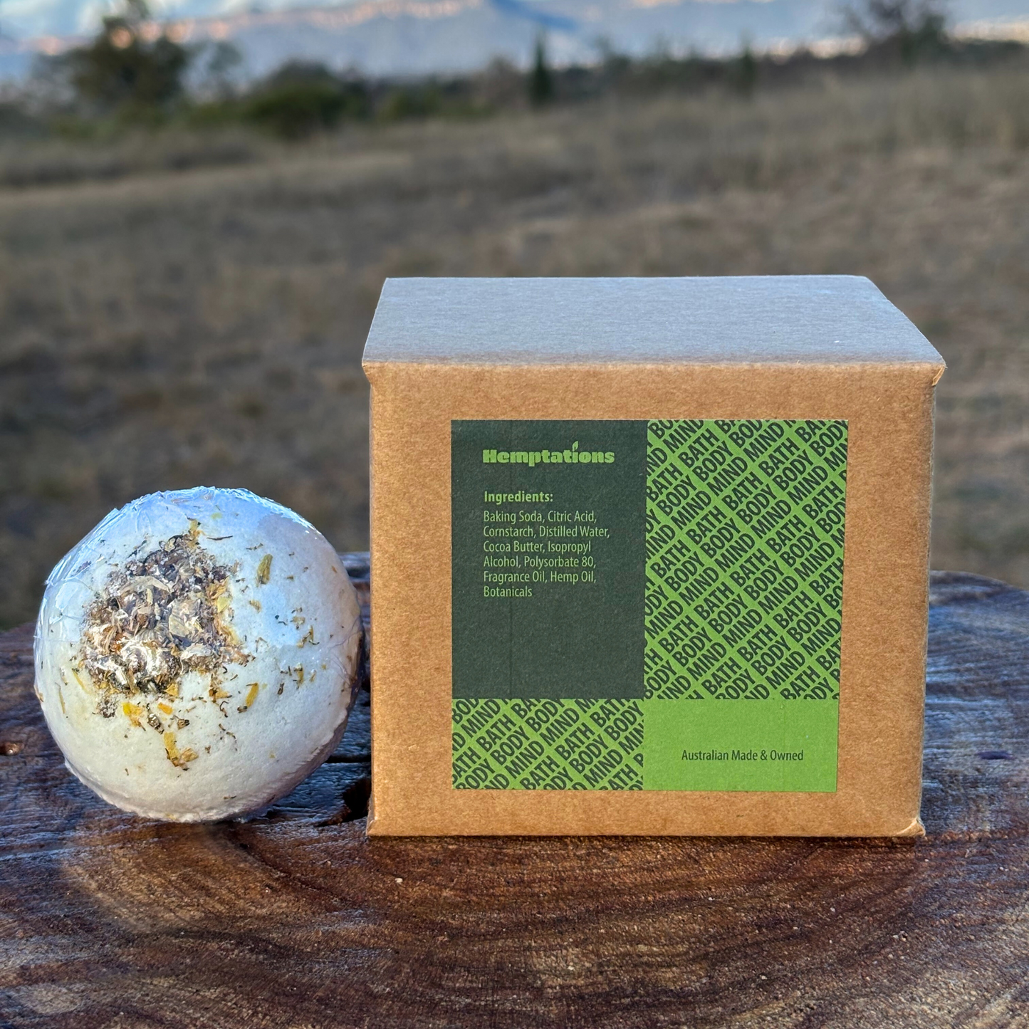Bath bomb with a box labeled 'Hemptations' on a wooden surface with a natural background.