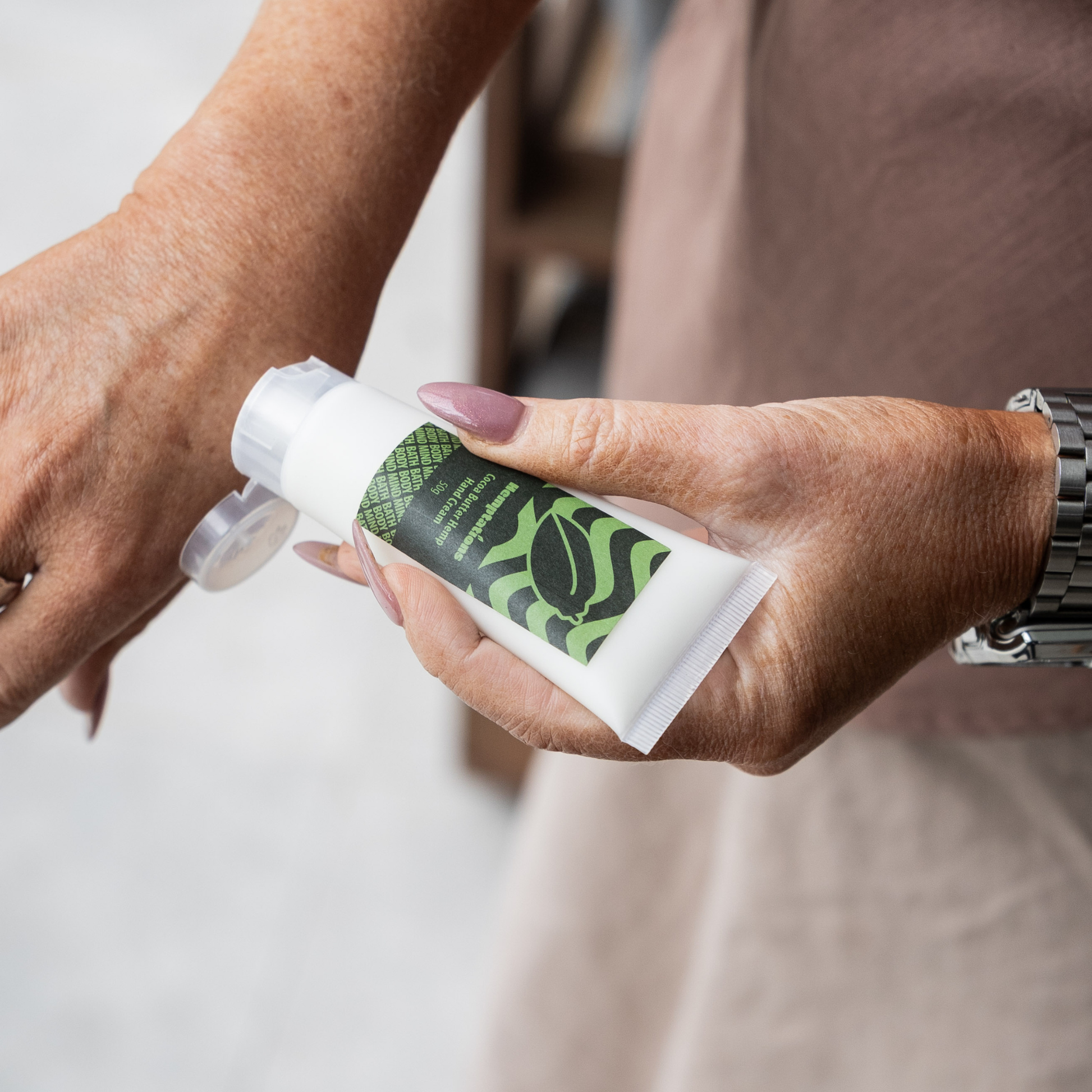 Hand holding a tube of hand cream with a green label.