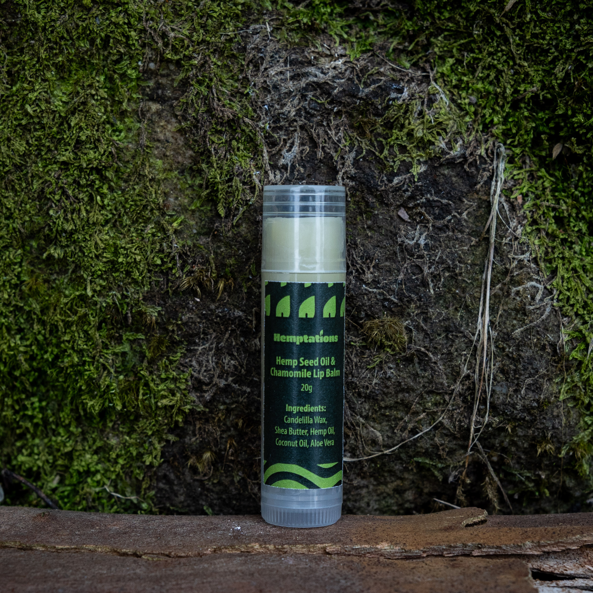 Lip balm tube with green label on a wooden surface and moss background