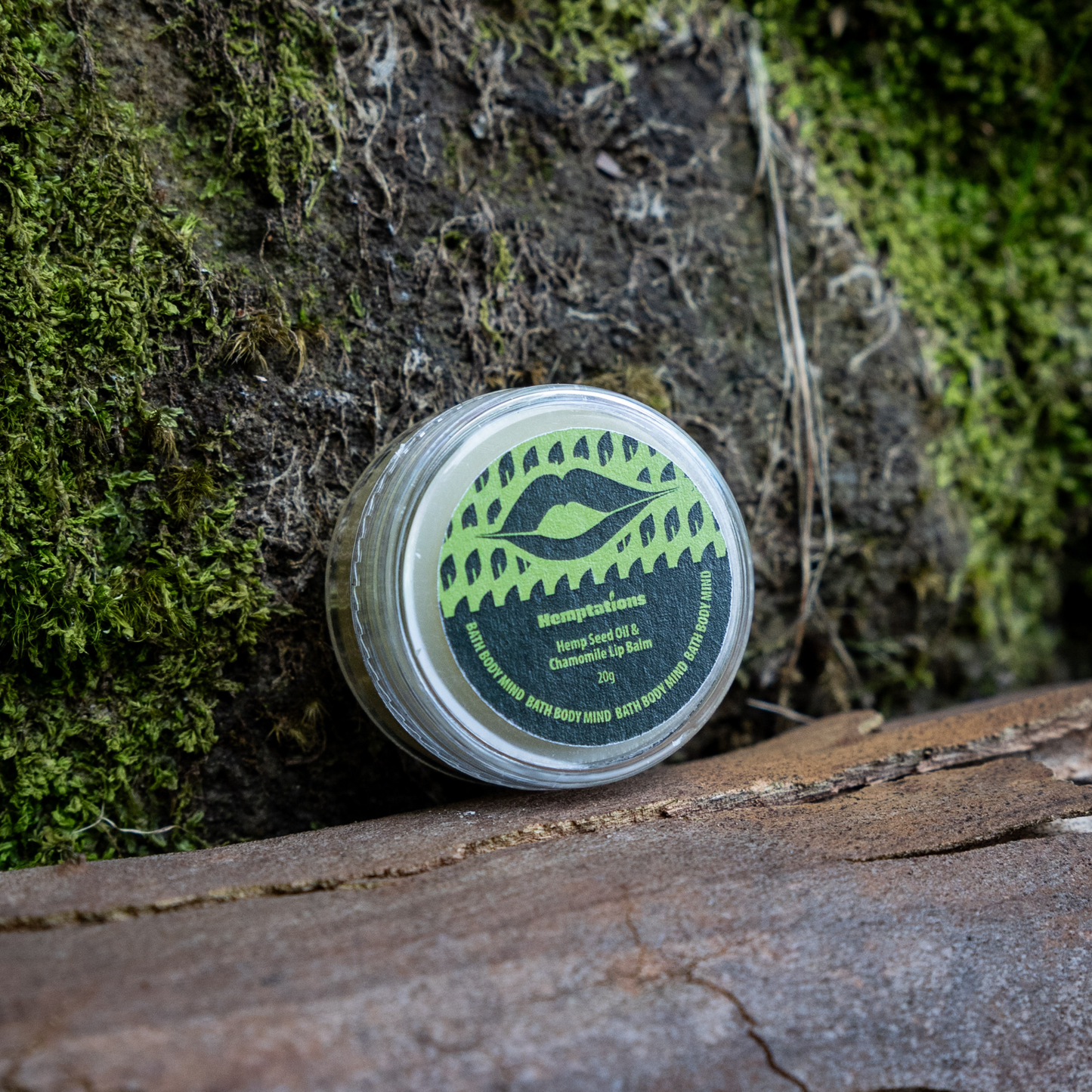 Lip balm container with green label on a mossy surface