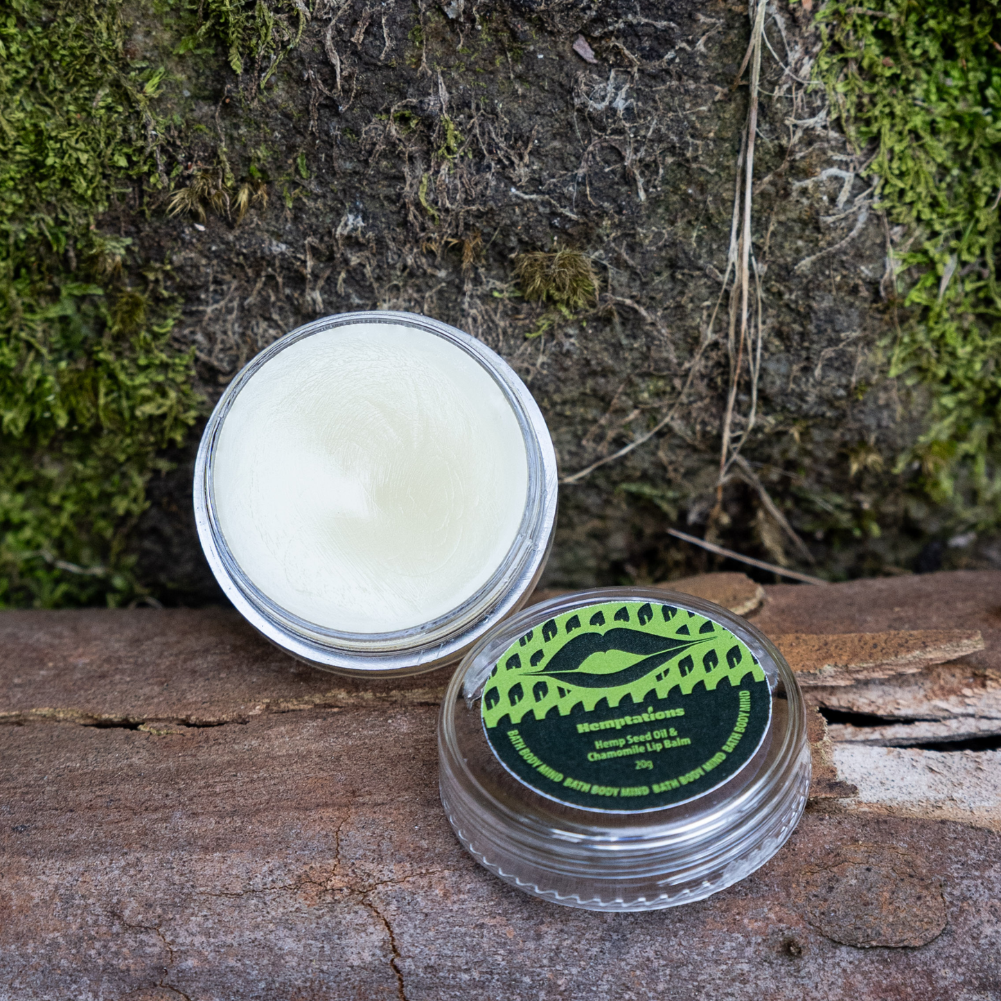 Open container of lip balm with a green label on a wooden surface with moss in the background