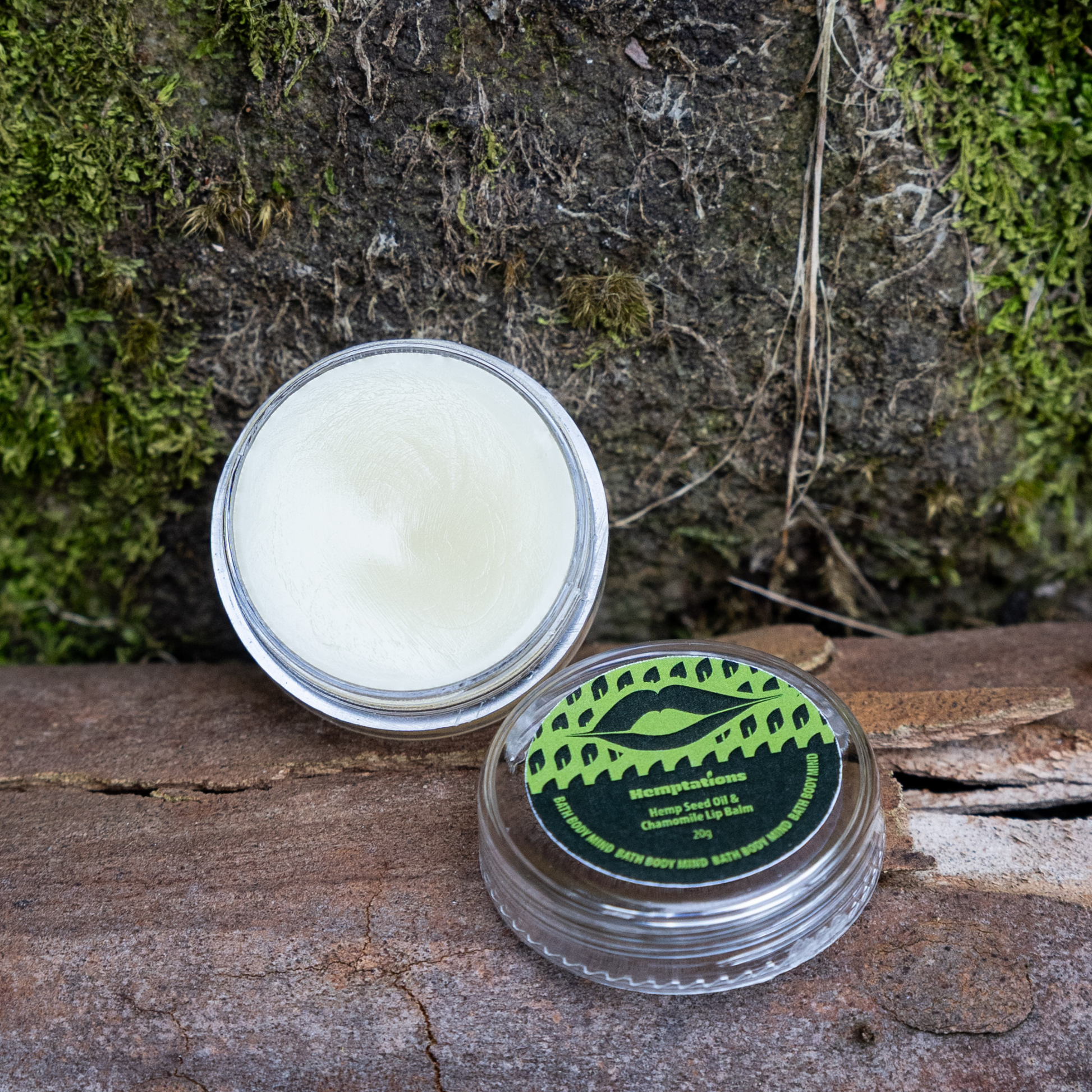 Open container of lip balm with a green label on a wooden surface with moss in the background